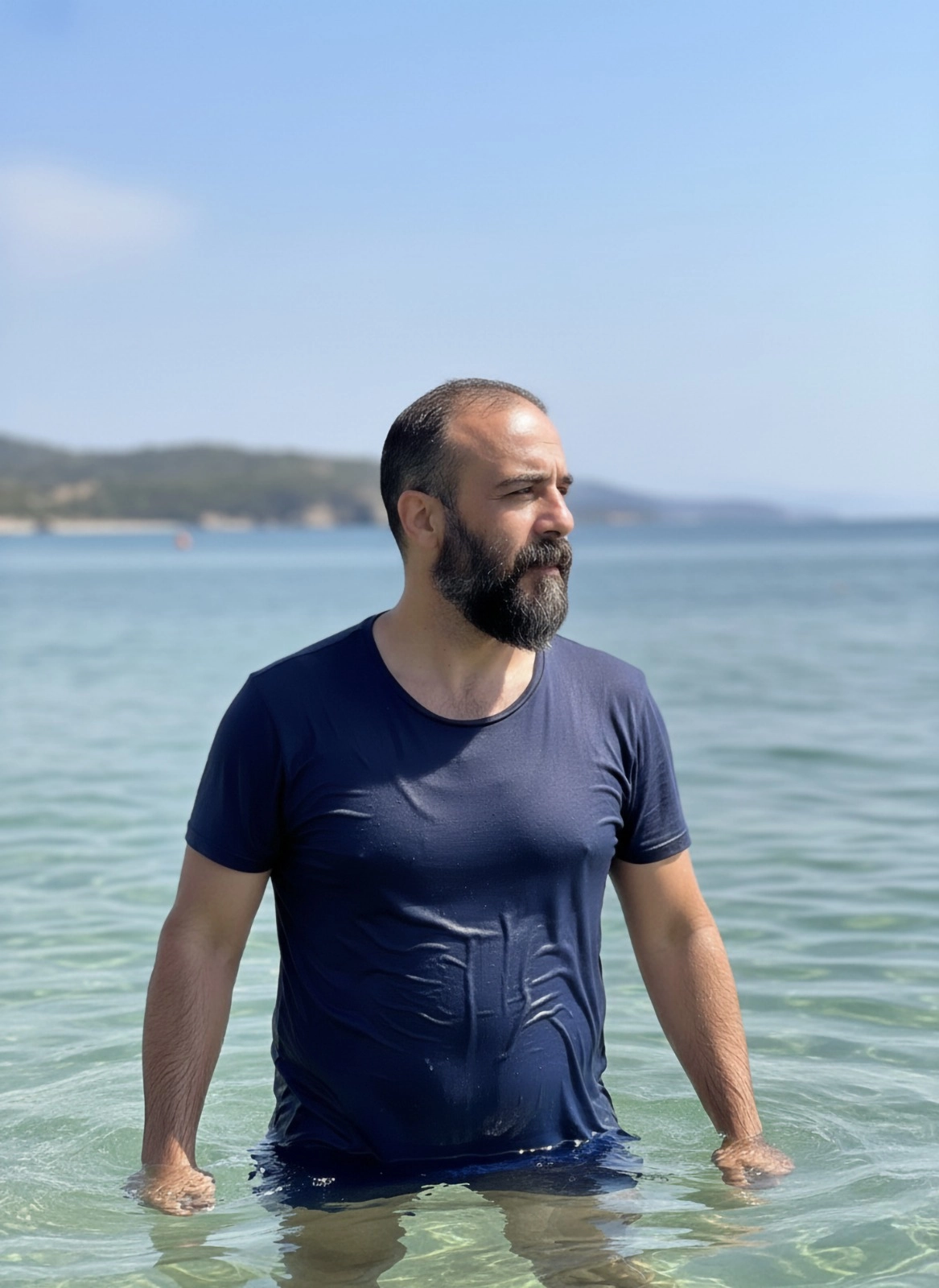 Мужчина в мокрой футболке по пояс в морской воде